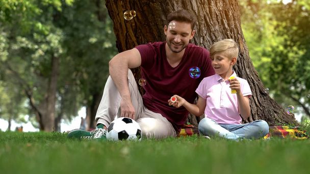 Father and boy enjoying making bubbles in park, family entertainment in weekend - Fotoğraf, Görsel