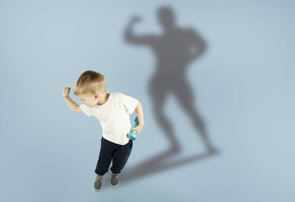 menino desportivo emocional com halteres mostra seus músculos em um fundo azul isolado. O conceito de um estilo de vida saudável
 - Foto, Imagem