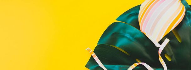 Tropical jungle palm monstera leaves and a woman's swimsuit top on bright yellow paper background. Summer vacations creative flat lay concept template for text. Long wide banner - Fotografie, Obrázek