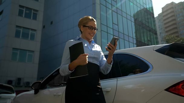 Woman in business suit smiling, reading email with good news on her smartphone - Photo, Image