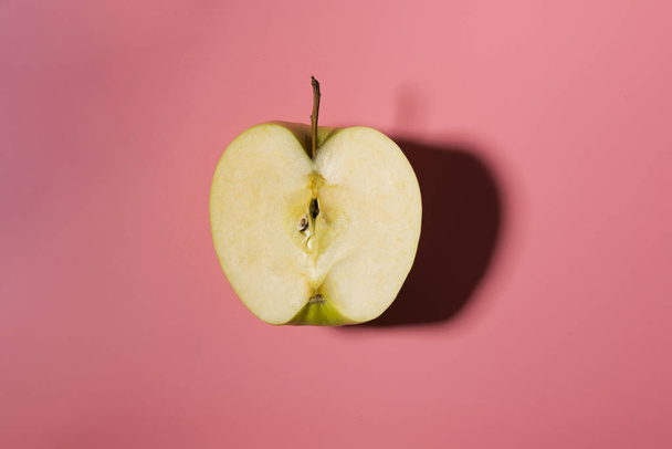 Sliced green delicious apple isolated on pink background with contrast shadows - Foto, imagen