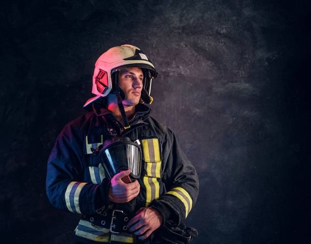 Portrait d'un pompier en uniforme et casque de sécurité tenant un masque à oxygène et regardant de côté avec un regard confiant
. - Photo, image
