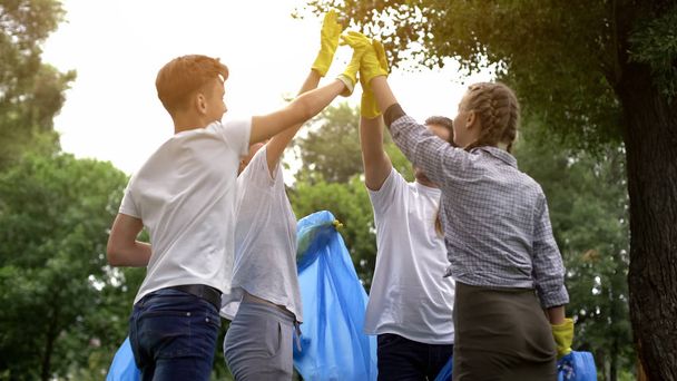 Team of volunteers hi-fiving during collecting garbage in park, save nature - Foto, Imagem