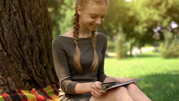 Teenager girl shopping online on tablet, inserting credit card number, sales - 写真・画像