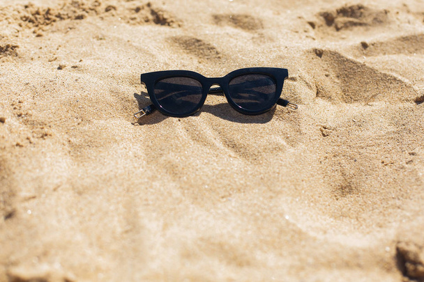Lunettes de soleil noires élégantes sur une plage ensoleillée et sablonneuse, vue sur le dessus avec espace pour copier. Vacances d'été et concept de voyage. Accessoires et essentiels modernes d'été
 - Photo, image