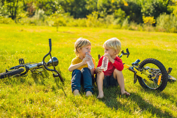 Two little boys drink water in the park after riding a bike. - Foto, imagen
