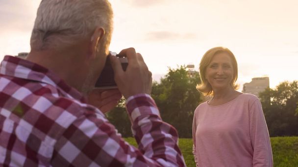 Man in his 50s photographing his beautiful wife in park at sunset, hobby, date - Foto, immagini