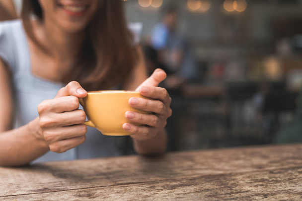 Cheerful asian young woman drinking warm coffee or tea enjoying it while sitting in cafe. Attractive happy asian woman holding a cup of coffee. - Photo, Image