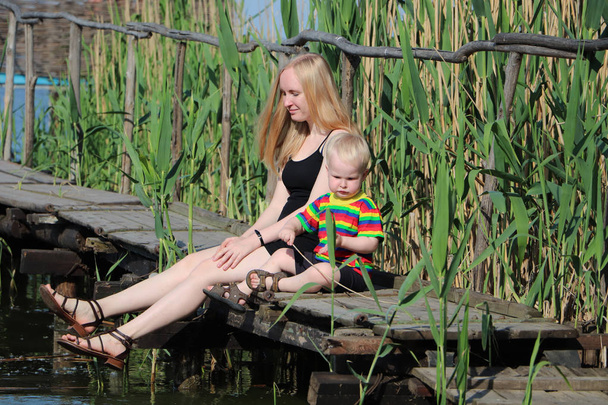 A young mother and son are resting on the bridge by the river. Lifestyle concept - Photo, Image