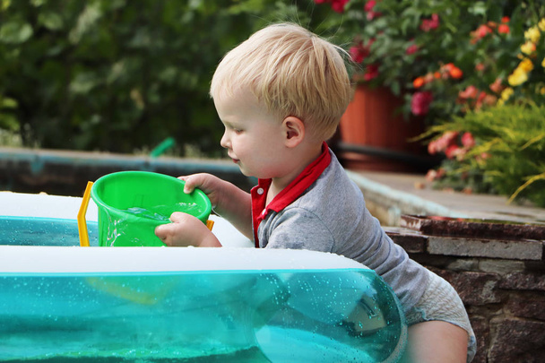 Маленький хлопчик грає з водою біля надувного басейну. Літні та сімейні канікули. Щасливе дитинство
 - Фото, зображення