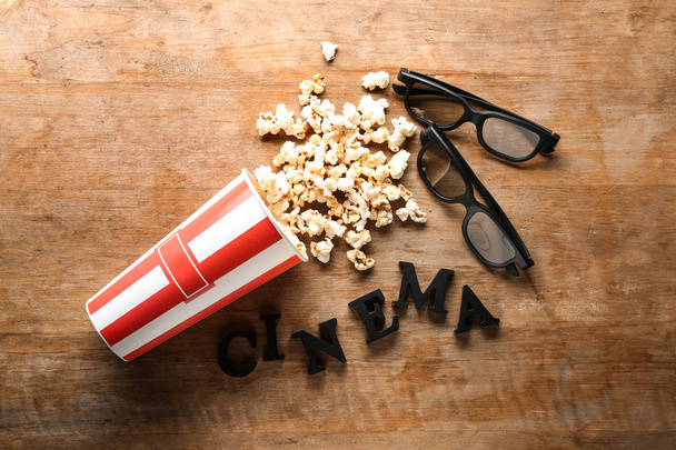 Перевернутая бумажная чашка вкусного попкорна, 3D очки и слово CINEMA на деревянном фоне
 - Фото, изображение