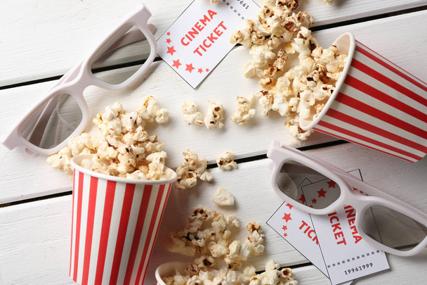 Převržený papírových kelímků chutná popcorn, vstupenky do kina a brýle na dřevěné pozadí - Fotografie, Obrázek
