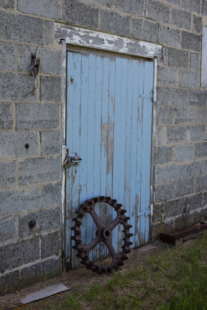 Roda de empacotador de aço vintage na frente de uma porta de celeiro antigo azul fora de Swift Current, Saskatchewan, Canadá
 - Foto, Imagem