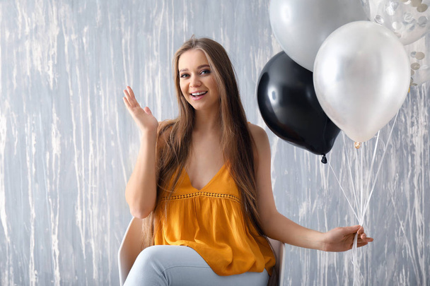 Beautiful young woman with balloons sitting on chair against grunge wall - Φωτογραφία, εικόνα