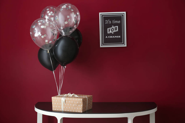 Mesa com balões de aniversário e caixa de presente perto da parede de cor
 - Foto, Imagem
