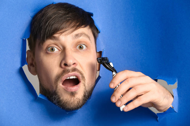 Шокированный человек с бритвой, видимой через отверстия в рваной цветной бумаге
 - Фото, изображение