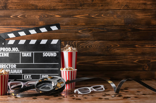 Filmklöppel mit Filmrolle, Popcorn und Gläsern auf Holztisch - Foto, Bild