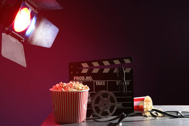 Movie clapper with film reel, popcorn and glasses on table - Foto, Imagen