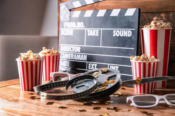 Movie clapper with film reel, popcorn and glasses on wooden table - Photo, Image