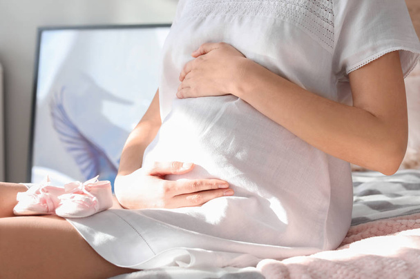 schöne schwangere Frau mit Babybooties im Schlafzimmer, Nahaufnahme - Foto, Bild