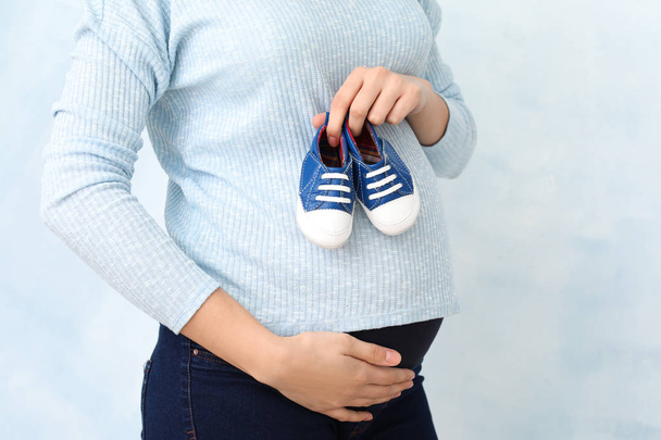 Hermosa mujer embarazada con zapatos de bebé en el fondo de color, primer plano
 - Foto, Imagen