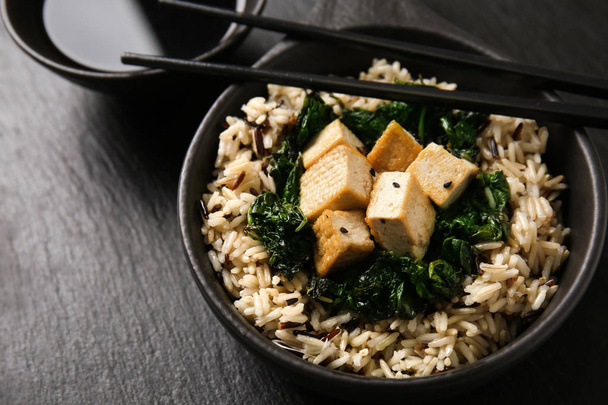 Tasty rice with tofu cheese in bowl on dark table - Photo, Image
