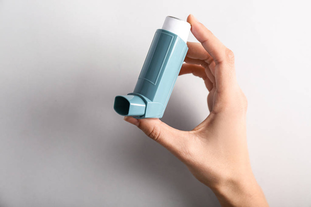 Female hand with inhaler against asthma on light background - 写真・画像