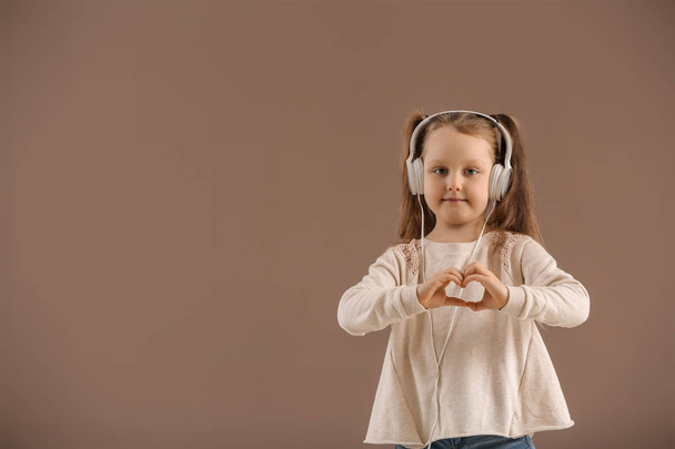 Cute little girl making heart with her hands while listening to music on color background - Foto, Imagen