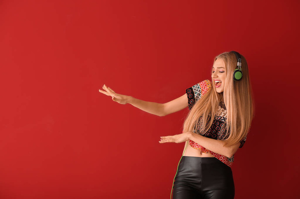 Beautiful young woman with headphones dancing against color background - Fotó, kép