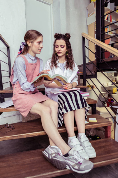 Fashionable tidy girls wearing sneakers while sitting on wooden stairs - Fotografie, Obrázek