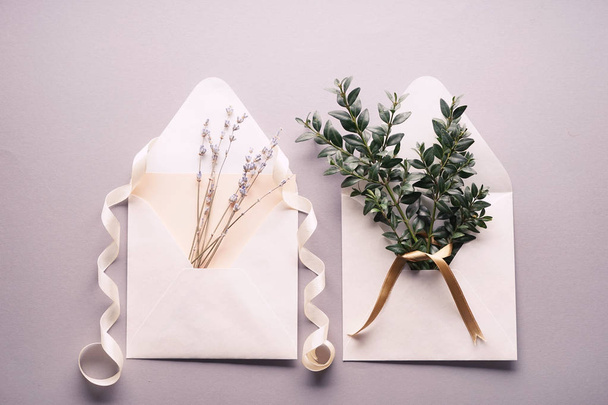 Envelopes de papel com ramos verdes, flores e decoração em fundo claro
 - Foto, Imagem