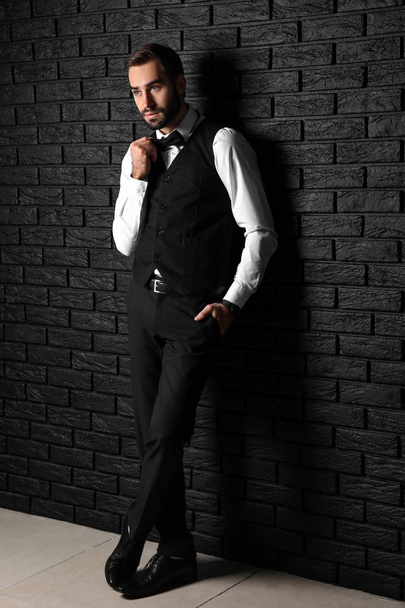 Bonito homem elegante perto de parede de tijolo escuro
 - Foto, Imagem