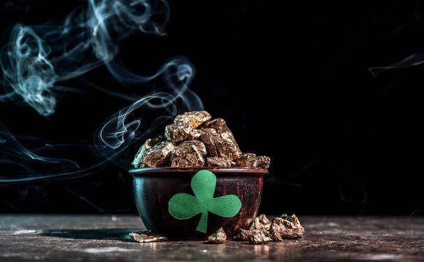 Leprechaun's pot with treasure on table against dark background. St. Patrick's Day celebration - Photo, Image