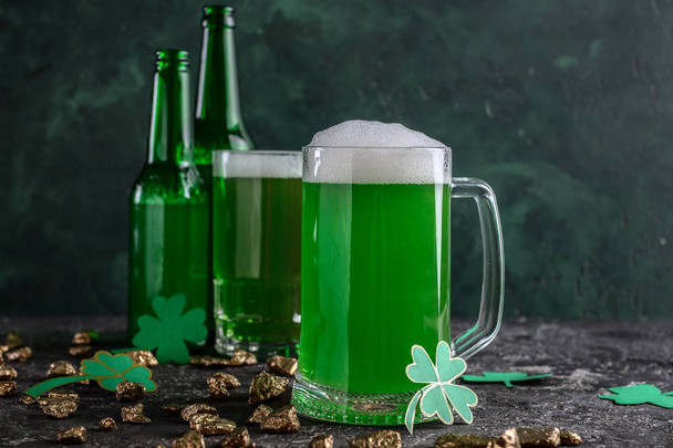 Mug of green beer with gold nuggets and clover on grunge table. St. Patrick's Day celebration - Фото, изображение