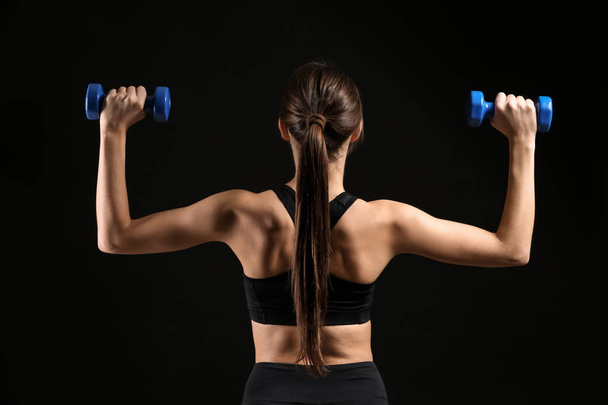 Sportos fiatal nő súlyzókkal sötét háttéren - Fotó, kép