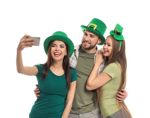 Jóvenes con sombreros verdes tomando selfie sobre fondo blanco. Celebración del Día de San Patricio
 - Foto, Imagen