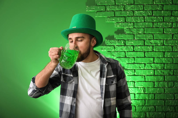 Όμορφος νεαρός άνδρας με το πράσινο καπέλο πίνοντας μπύρα σε έγχρωμο φόντο. Εορτασμός της ημέρας του Αγίου Πατρικίου - Φωτογραφία, εικόνα
