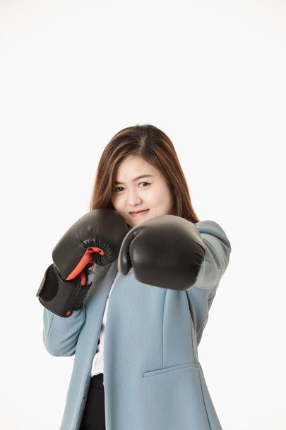 Close-up studio portrait of young, beautiful, attractive Asian lady, in light blue business suit, put on black leather boxing gloves, playfully posing for fighting action, on isolated white background - Photo, Image