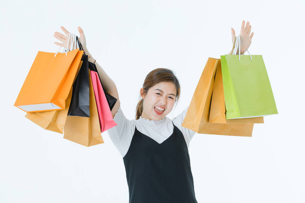 Fiatal vonzó, ázsiai nő fehér pólóban, partedli overál ruha, mosolygós, tartja a vásárolt áruk sok többszínű papír bevásárló táskák elszigetelt fehér háttér. - Fotó, kép