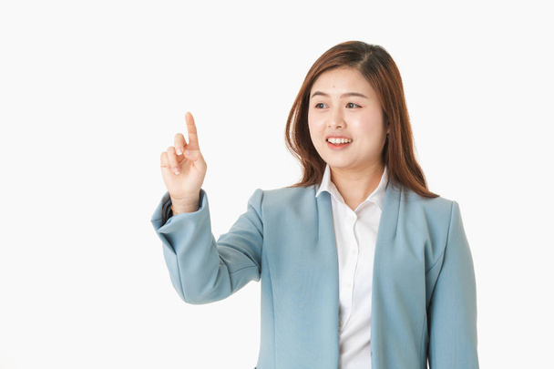 Close-up studio portrait of young, beautiful, attractive Asian lady in white shirt, pastel blue business suit     smiling, touching invisible screen or touch board, on isolated white background - Photo, Image