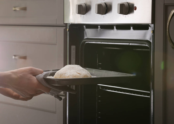 Vrouw zetten bakplaat met rauwe deeg voor een brood in de oven - Foto, afbeelding