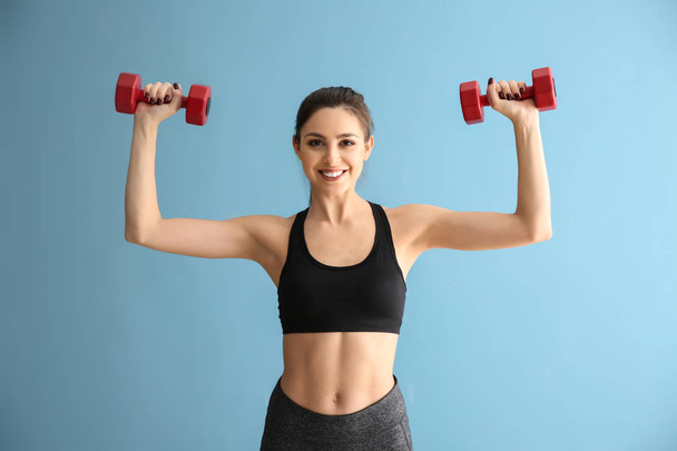 Sporty young woman with dumbbells on color background - Foto, Imagem