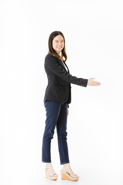 Aufnahme einer jungen, schönen, asiatischen Dame, langes schwarzes Haar, elegant lässig, stehend, lächelnd und Hand in Hand zur Begrüßung und Willkommensgeste, auf isoliertem weißem Hintergrund - Foto, Bild