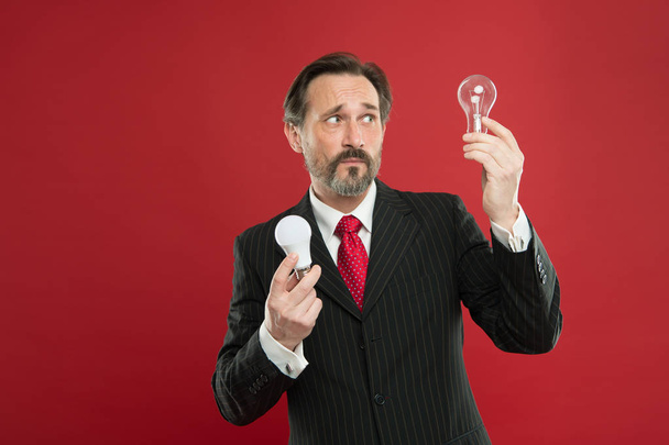 Lighting choices to save money. Man bearded consultant formal suit hold light bulb on red background. Symbol of idea progress and innovation. Environment friendly lighting. Energy efficient lighting - Φωτογραφία, εικόνα