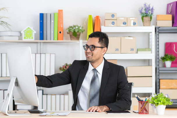 Retrato de jovem, bonito, asiático, homem de negócios, vestindo óculos, em terno de negócios, verificando relatório diário no computador em sua mesa de trabalho com fundo de escritório de inicialização
 - Foto, Imagem