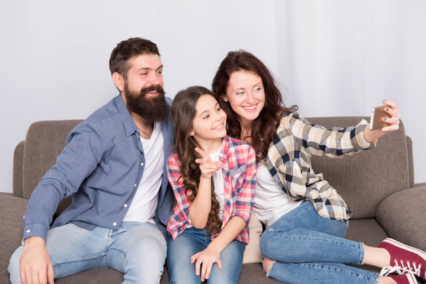 Capture happy moments. Family selfie. Family spend weekend together. Use smartphone for selfie. Friendly family having fun together. Mom dad and daughter relaxing on couch. Family posing for photo - Фото, изображение