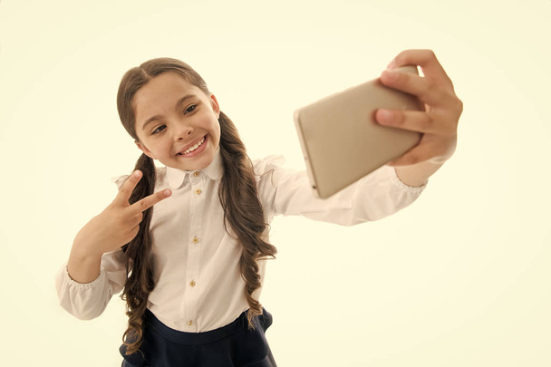 Happy girl take selfie isolated on white. Child smile with victory hand gesture on smartphone. digital marketing in virtual world. Selfie fun. Cute blogger make video call. Modern life and technology - Foto, afbeelding