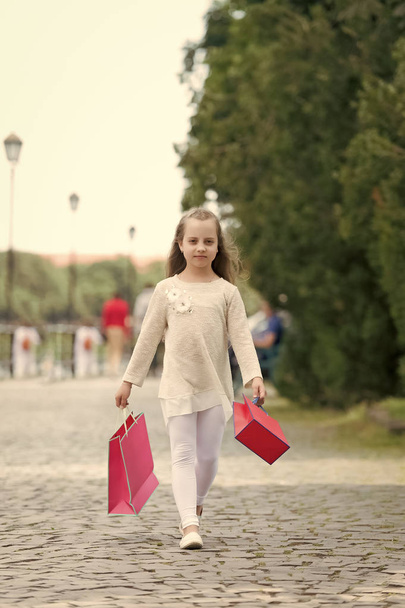 Girl shopping on calm face carries shopping bags, urban background. Kid girl with long hair fond of shopping. Shopping concept. Girl likes to buy clothes. Fashionista girl shopping with pink bags - Foto, imagen