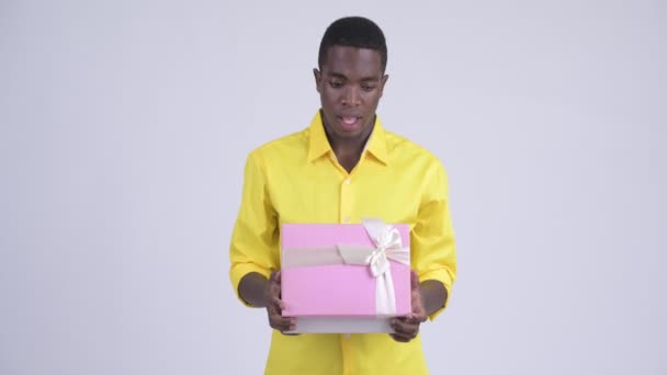 Young happy African businessman opening gift box and looking surprised - Felvétel, videó