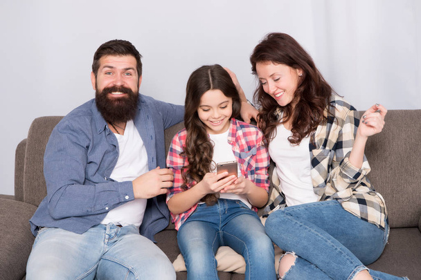Parental advisory. Family spend weekend together. Child little girl use smartphone with parents. Friendly family having fun together. Mom dad and busy daughter relaxing on couch. Family leisure - Foto, Bild